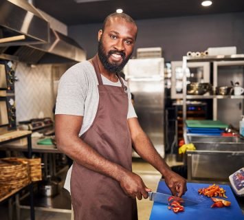 happy-young-chef-cutting-vegetables-in-restaurant-2023-11-27-05-25-08-utc.jpg
